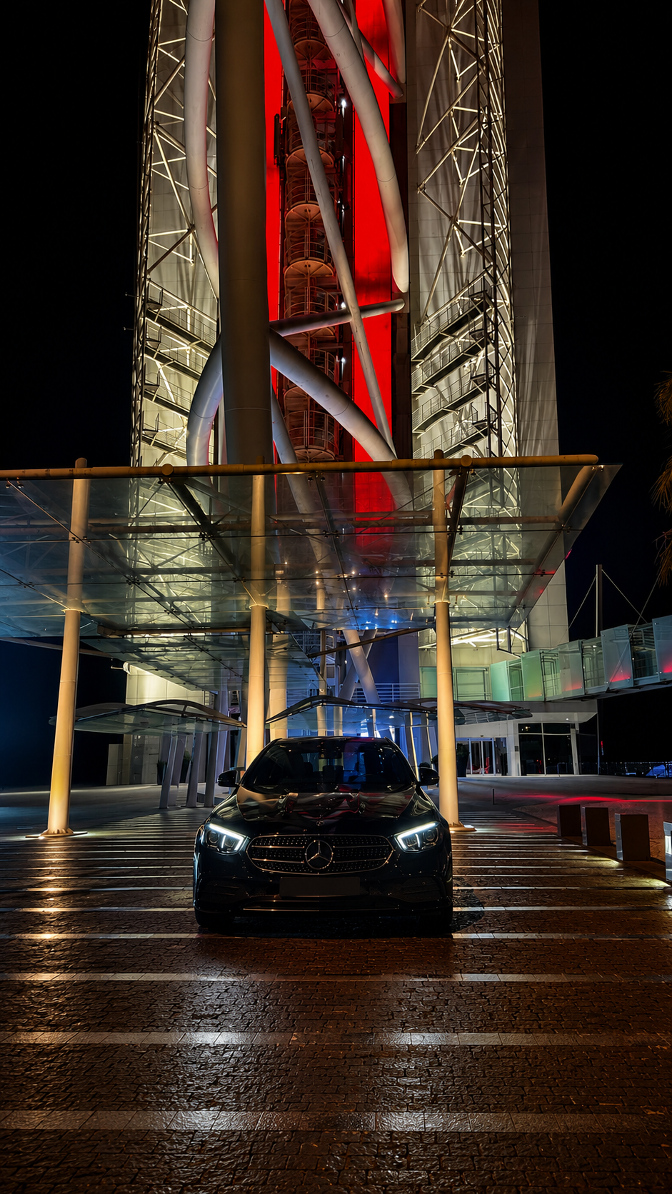 Mercedes Classe E preto sob torre iluminada em vermelho à noite